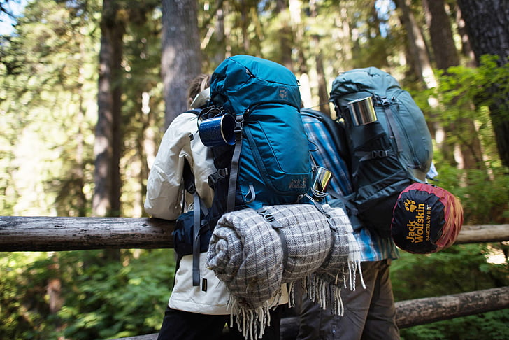 A backpack filled with hiking essentials including a Fenix flashlight, map, and water bottle against a scenic wooded backdrop..