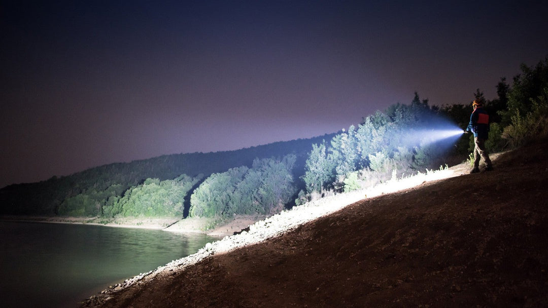 Person standing on a hill shining a bright flashlight on a lake and trees