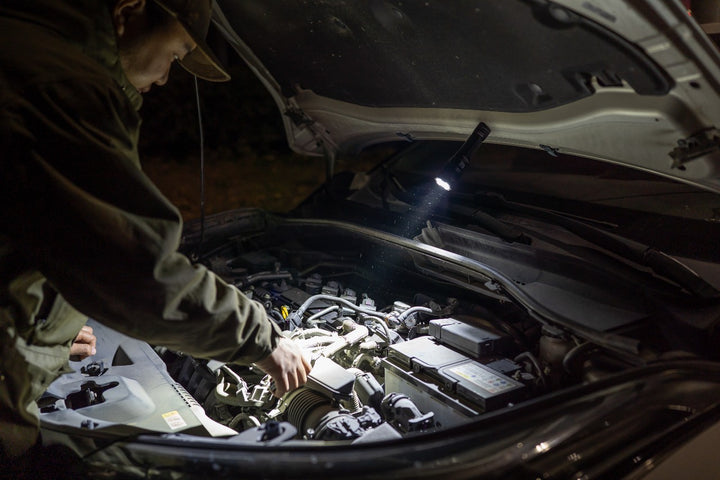 Person working under the hood of a car using the magnetic tail cap of the Fenix C7 Pro Quick-Charging Work Flashlight 