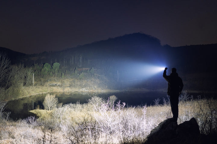 Person holding a Fenix C7 Pro Quick-Charging Work Flashlight in a dark landscape with mountains and a lake.