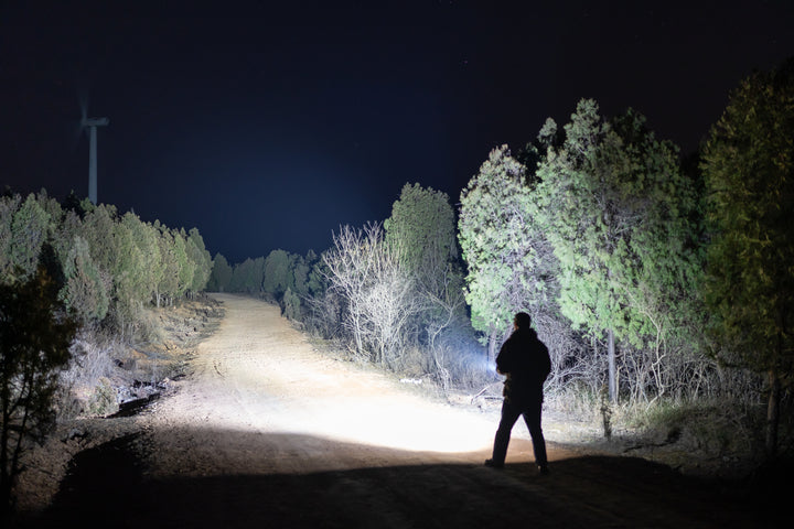 Person standing on a dark forest path illuminated by a Fenix C7 Pro Quick-Charging Work Flashlight 