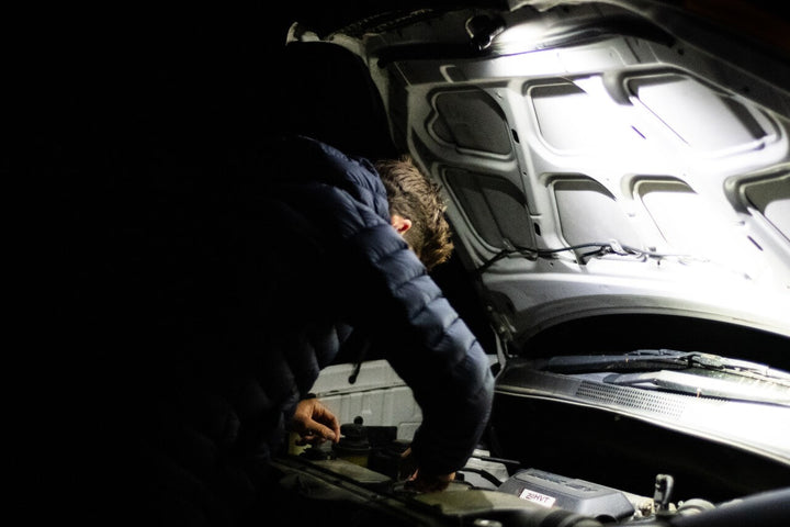Person working on a car engine with the hood open at night, using the Fenix HM53R headlamp magnetic tail cap.