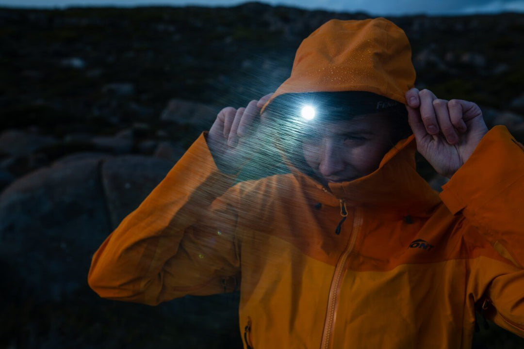 Person wearing an orange raincoat with a Fenix HM53R headlamp in a dark, rocky landscape