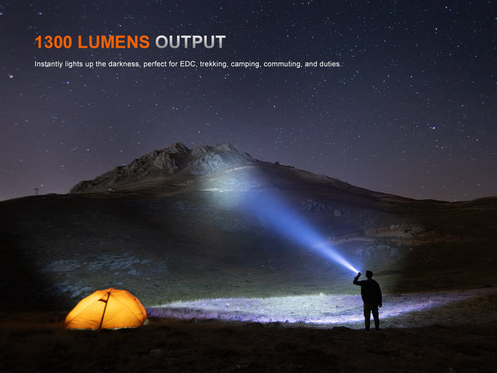 Person holding a Fenix PD26R ACE Customizable Compact Flashlight illuminating a mountainous landscape with a tent, featuring 1300 lumens output text.