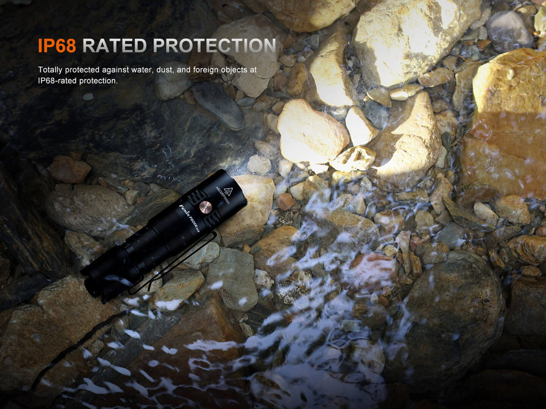 Black Fenix PD26R ACE Customizable Compact Flashlight on rocks with water, highlighting IP68 rating.