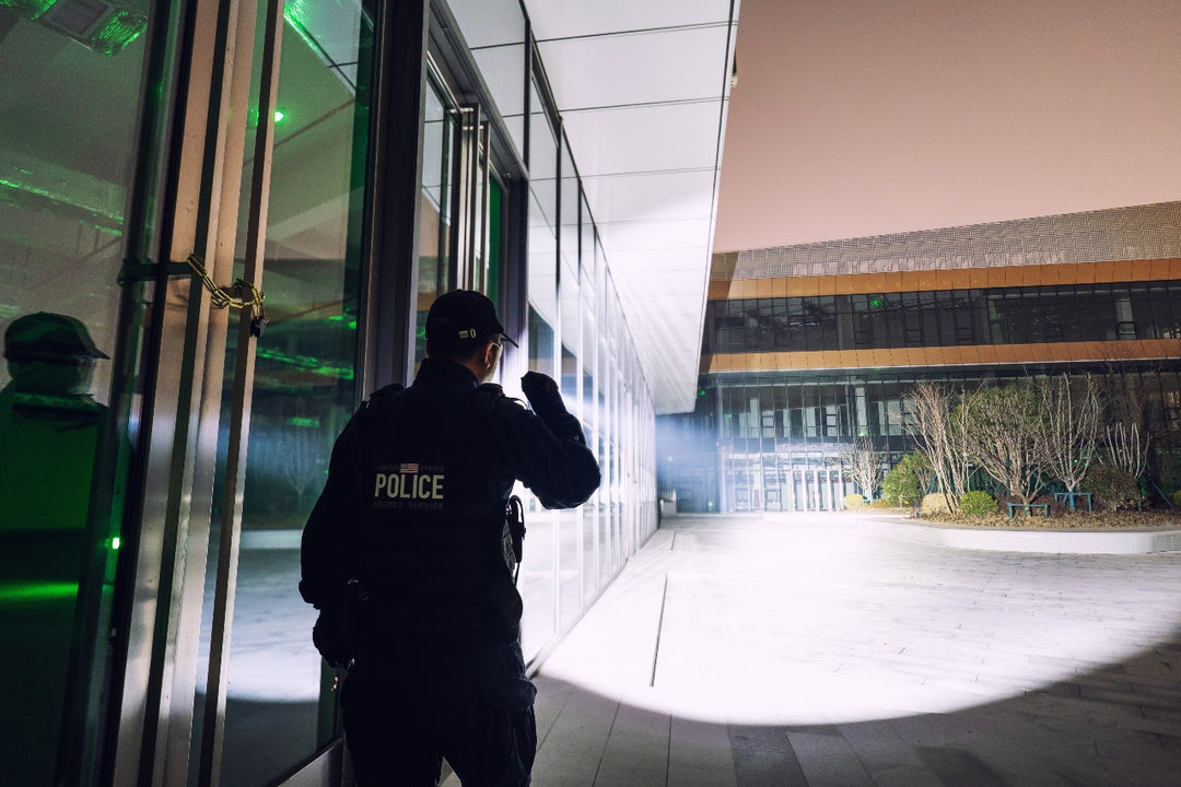Person in police uniform using a Fenix TK15R adaptive flashlight outside a building