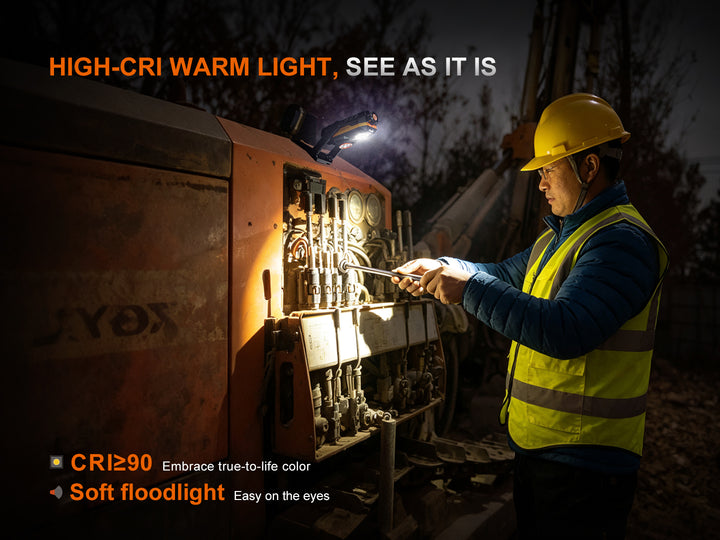 Worker in a hard hat using the Fenix WT26RM's high-CRI floodlight (CRI ≥90) to inspect wiring inside heavy machinery at night, showing true-to-life color rendering
