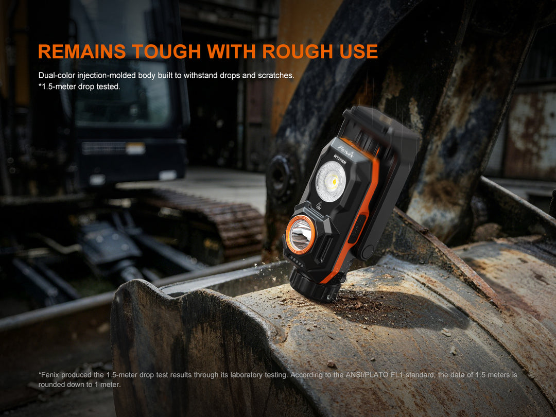 Fenix WT26RM work light resting on a dirt-covered excavator bucket, illustrating its impact-resistant dual-color injection-molded housing