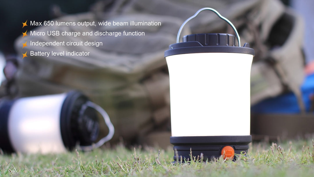 Fenix CL30R LED camping lantern sitting in grass with a backpack in the background