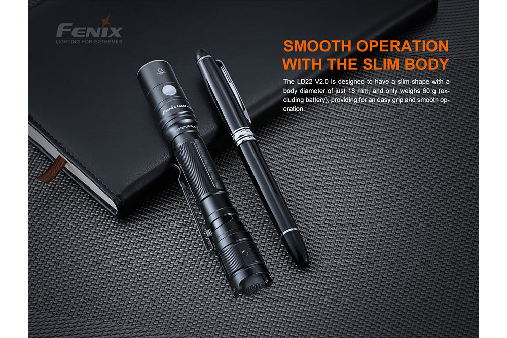 Fenix LD22 V2 compact LED flashlight resting on a book next to a pen to show its slim body