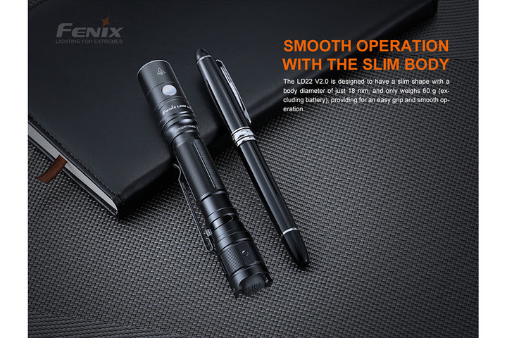 Fenix LD22 V2 compact LED flashlight resting on a book next to a pen to show its slim body