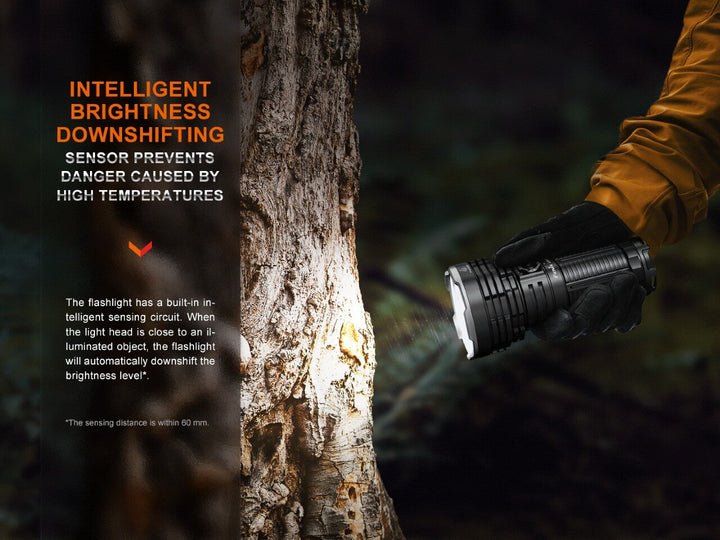 Fenix LR40R V2 rechargeable LED searchlight held close to a tree, activating its intelligent downshift mode