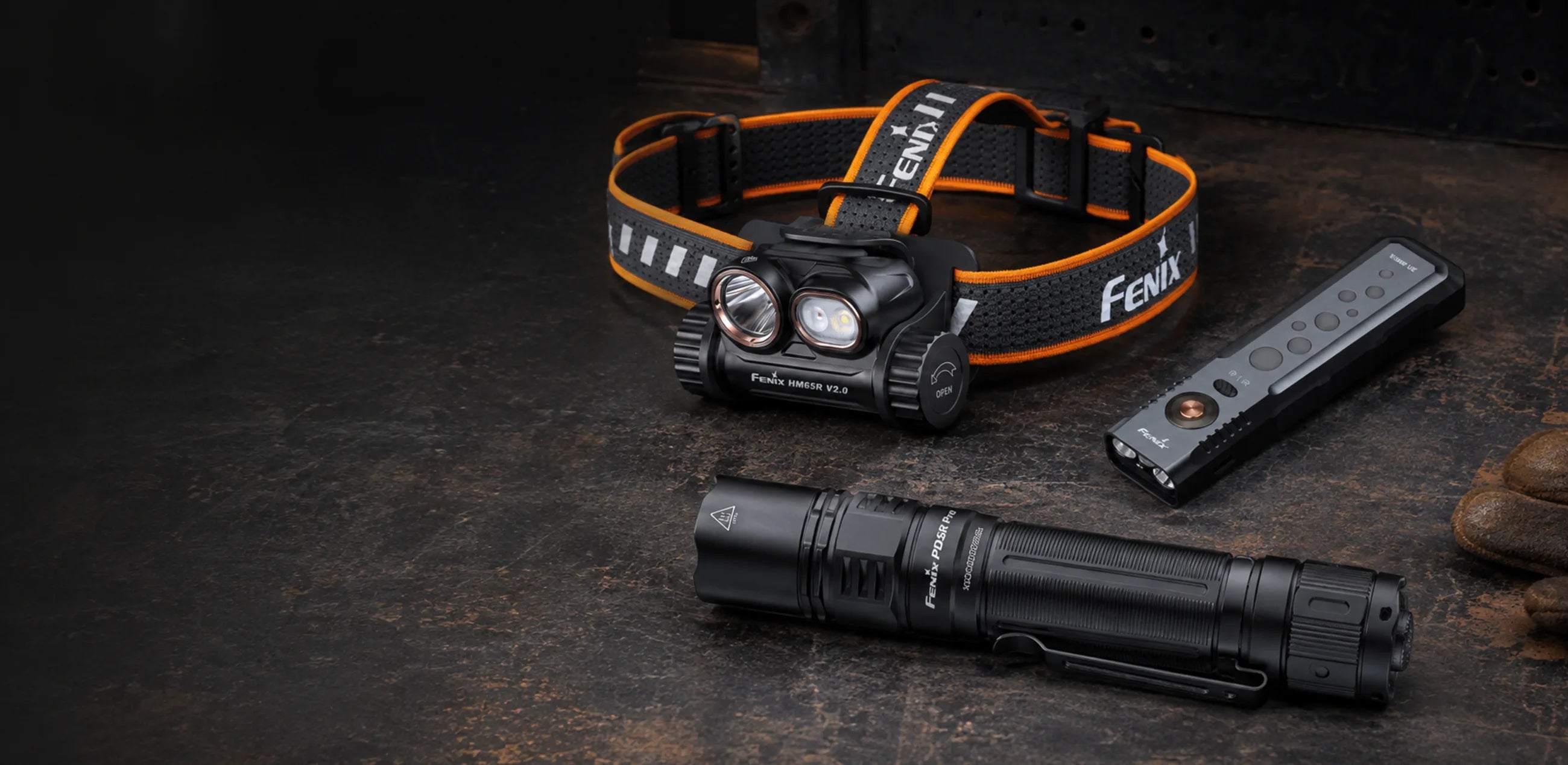 Fenix PD36R Pro flashlight, HM65R V2.0 headlamp, and E08R UE light arranged on a dark industrial workbench